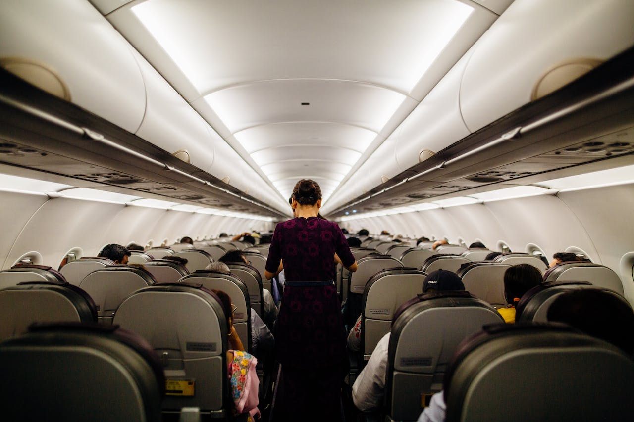 Na obrazku widoczna jest stewardessa w eleganckim uniformie obsługująca pasażerów w samolocie